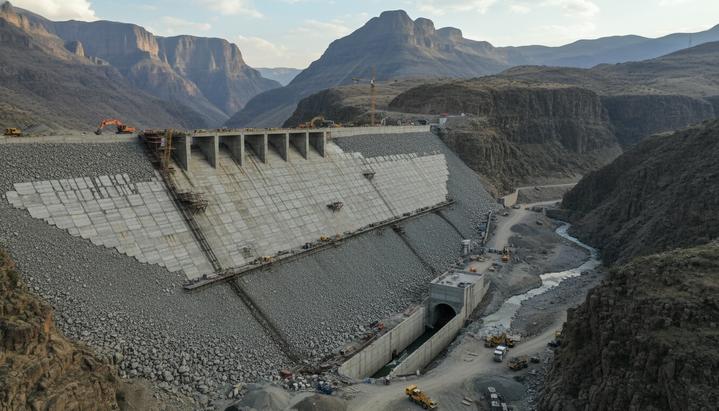 Масштабное строительство каменно-набросной плотины Полихали в скалистом ущелье Лесото. Частично возведенная дамба и река в долине.